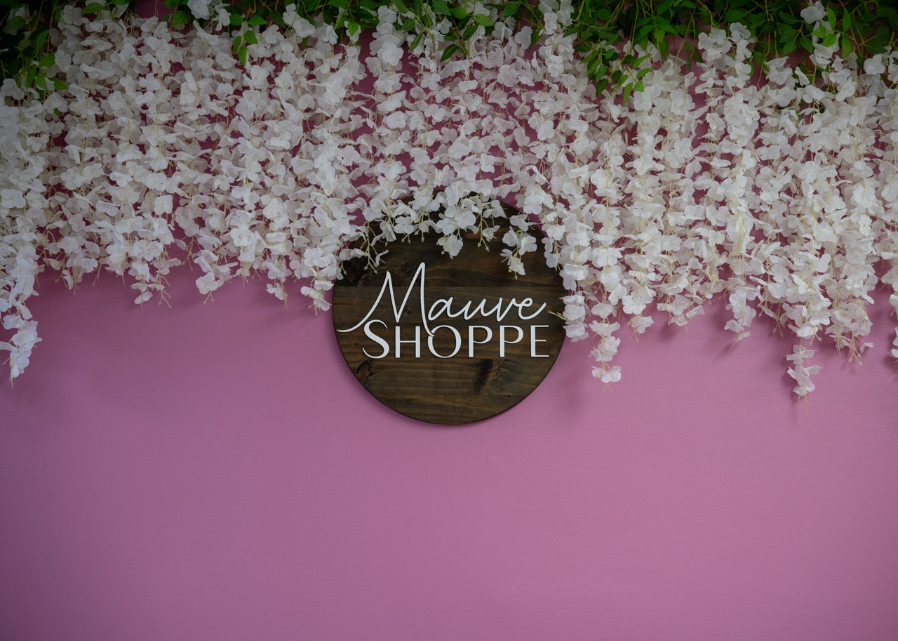 Wooden sign with 'Mauve Shoppe' on a pink background with white flowers.